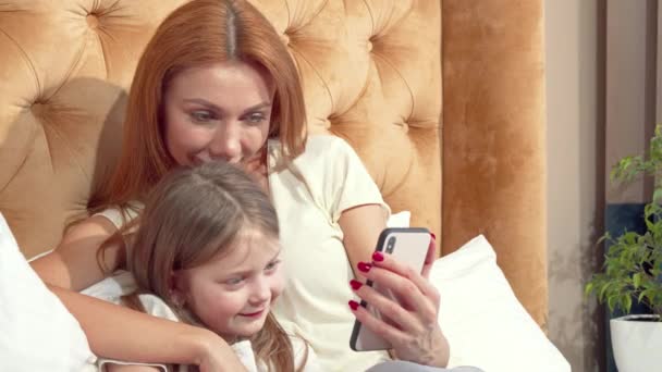 Hermosa mujer y su linda hija pequeña usando el teléfono inteligente en casa juntos — Vídeos de Stock