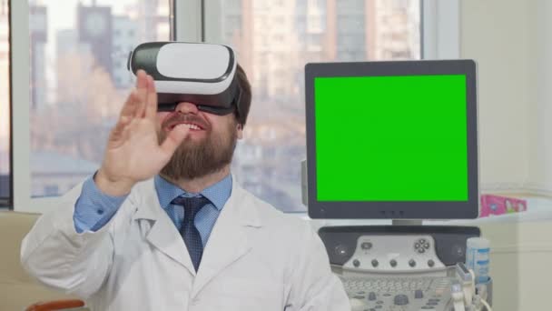 Bearded doctor wearing 3d vr glasses, computer with green screen on the back — Stock Video