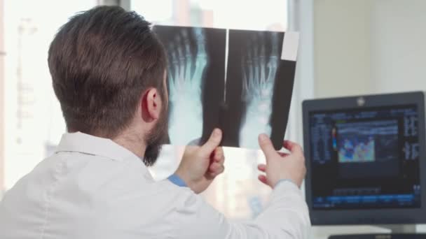 환자의 발 엑스레이를 보고 있는 남성 의사의 후방 시야 샷 — 비디오