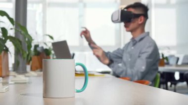 Masada kahve fincan, arka planda çalışma 3D VR gözlük kullanarak adam