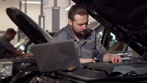 Trabajador de servicio de coche usando el ordenador portátil, examinando el motor de un coche — Vídeos de Stock