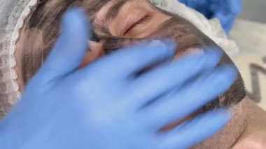 Erkek müşterinin yüzüne siyah maske uygulayan güzellik uzmanı