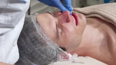 Profesyonel kozmetolojist pamuk ped ile bir erkek müşterinin cilt temizleme