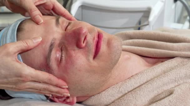 Przystojny człowiek uśmiechnięty do aparatu, odbieranie masaż twarzy w centrum spa — Wideo stockowe