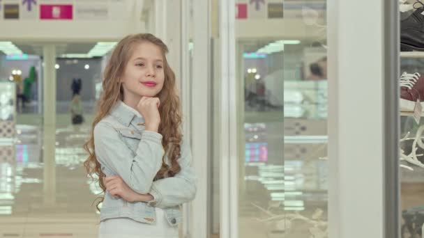 Cute little girl smiling to the camera, examining fashion store display — Stock Video