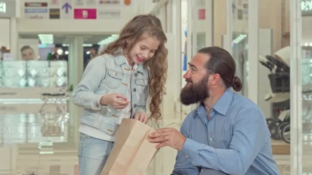 Schattig klein meisje en haar vader kijken naar binnen boodschappentassen in het winkelcentrum — Stockvideo