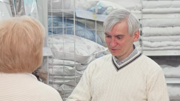 Старший мужчина выбирает постельные принадлежности со своей женой в магазине мебели — стоковое видео