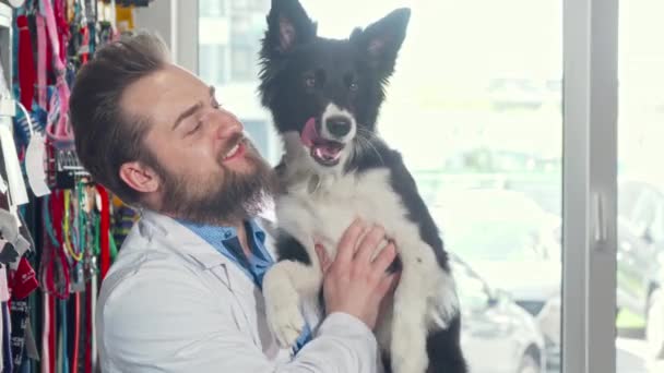 Fröhlicher bärtiger Tierarzt streichelt liebenswerten Hund in seiner Klinik — Stockvideo