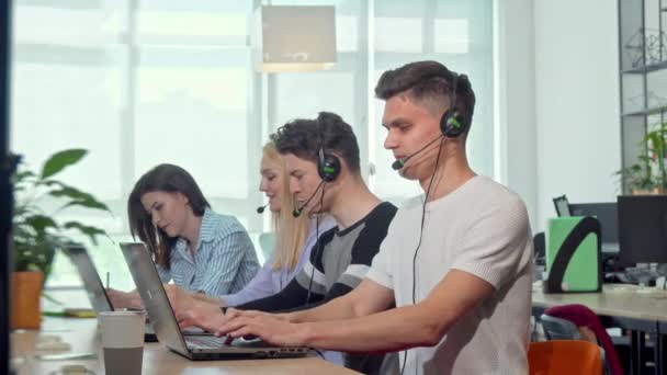 Friendly young man smiling to the camera, working at customer support call center — Stock Video