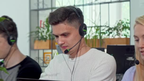 Joven trabajando en el centro de atención al cliente, usando auriculares — Vídeo de stock