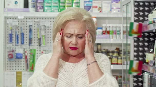 Senior woman having headache, looking for medicine at pharmacy — Stock Video