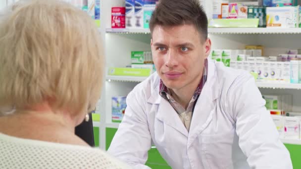 Atractivo joven químico masculino sonriendo, hablando con su cliente senior — Vídeos de Stock