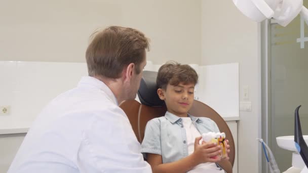 Dentista maduro sonriendo a la cámara mientras trabaja con un niño adorable — Vídeo de stock