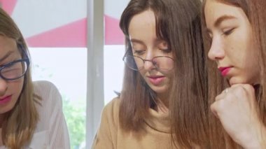 Sevimli genç kız kameraya gülümseyerek, arkadaşlarıile ev ödevi yapıyor