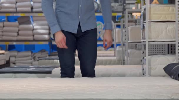 Hombre guapo eligiendo colchón ortopédico, acostado en una cama nueva en la tienda — Vídeo de stock