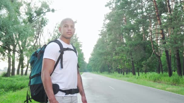 Bonito homem africano batendo na estrada rural com mochila — Vídeo de Stock