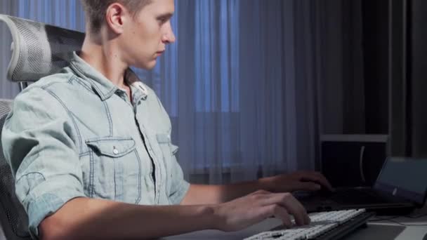 Captura deslizante de un freelancer masculino trabajando hasta tarde en la noche usando dos computadoras — Vídeos de Stock