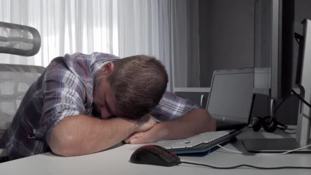 コンピュータで作業を終えた後、机の上で眠っている男 — ストック動画