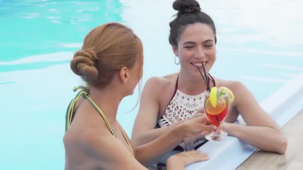 Twee prachtige vrouwen praten en drinken cocktails bij het zwembad — Stockvideo