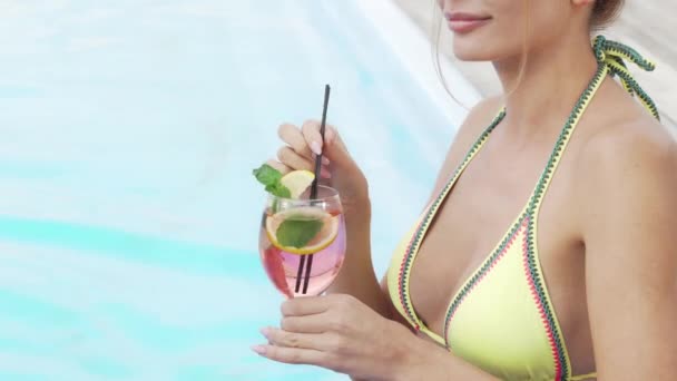 Bijgesneden schot van een sexy vrouw in een bikini nippen cocktail in de buurt van het zwembad — Stockvideo