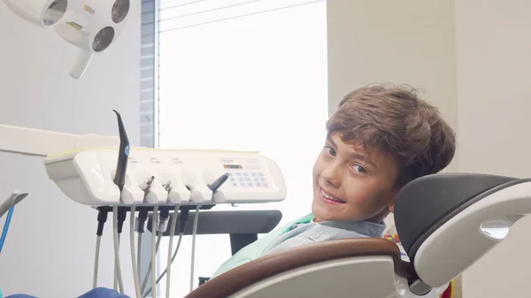 Charming young boy smiling to the camera, sitting in dental chair — Stock Photo, Image