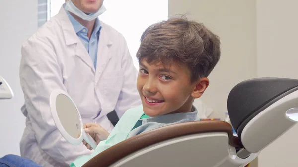 Kleiner Junge lächelt in die Kamera, nachdem er seine gesunden Zähne im Spiegel untersucht hat — Stockfoto