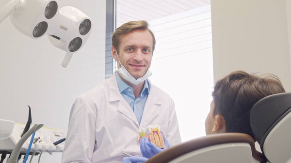 Cheerful mature male dentist smiling to the camera while educating little patient
