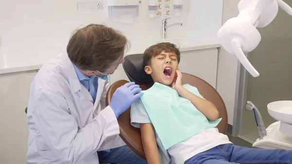 Mały chłopiec mający tootache, siedzący w fotelu dentystycznym podczas badania zębów — Zdjęcie stockowe