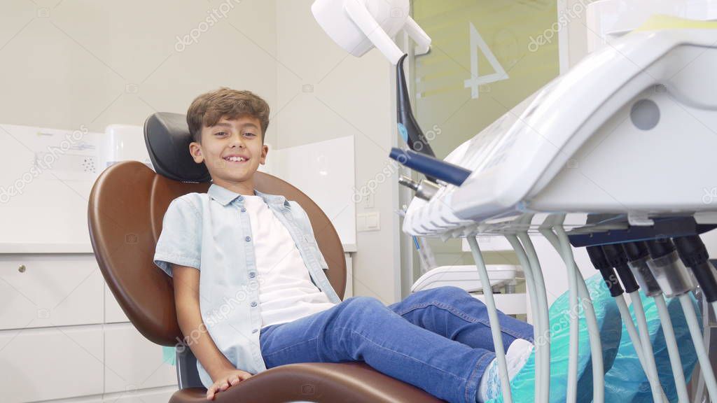 Lovely young boy sitting in dental chair waiting for teeth examination