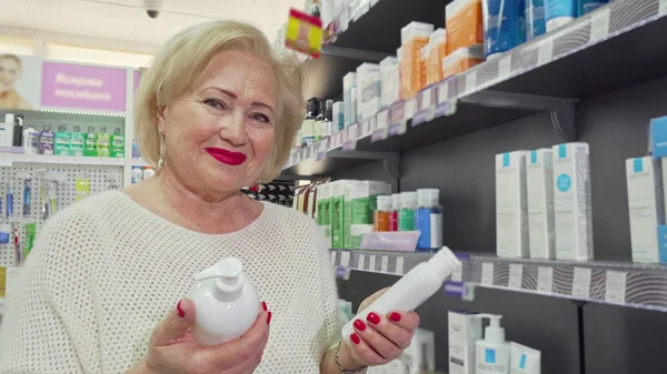 Mujer mayor encantadora sonriendo, eligiendo entre dos productos en la farmacia — Foto de Stock