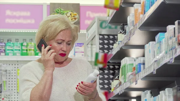 Mujer mayor hablando por teléfono mientras va de compras a la farmacia — Foto de Stock