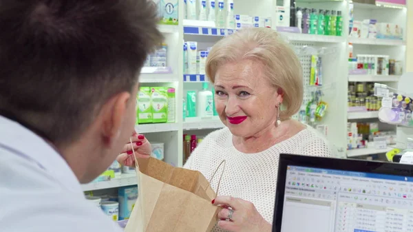 Eczaneden tıbbi ürünler alan kıdemli kadın, alışveriş çantasına bakıyor