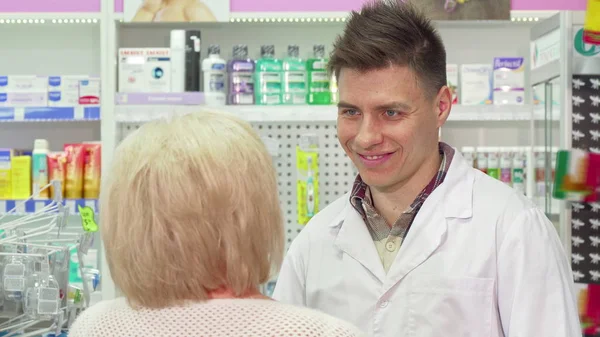 Unga manliga apotekare pratar med sin äldre klient — Stockfoto