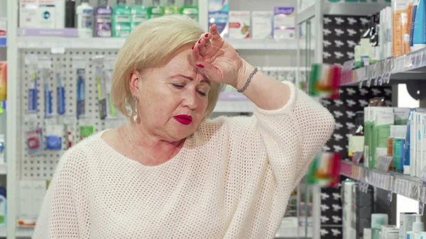 Mujer mayor sintiéndose enferma, buscando medicamentos en la farmacia local — Foto de Stock