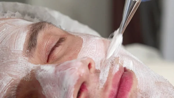 Schiebebild eines Mannes, der sich von Kosmetikerin im Kurzentrum eine Gesichtsmaske aufsetzen lässt — Stockfoto
