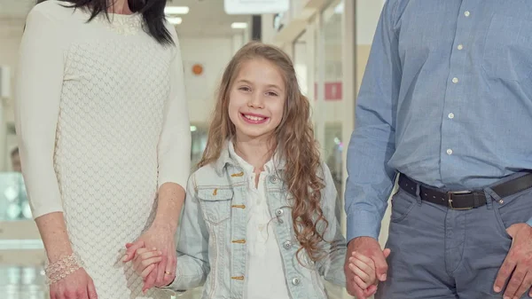 Linda niña sonriendo a la cámara, cogida de la mano con sus padres —  Fotos de Stock