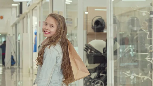 ショッピングモールで買い物袋を持って、カメラに微笑む幸せな小さな女の子 — ストック写真