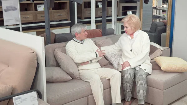 Elderly husband and wife trying new sofa, shopping for furniture