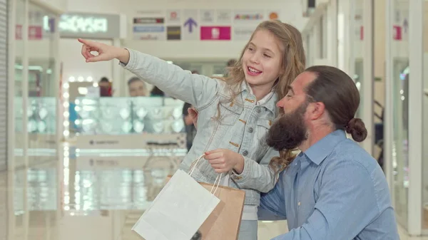 Klein meisje wijst weg, toont iets aan haar vader in het winkelcentrum — Stockfoto