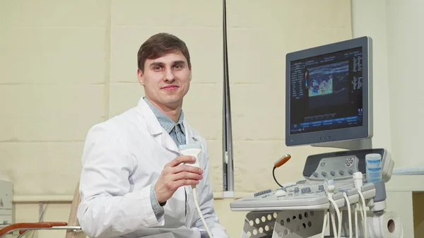 Beau médecin joyeux souriant à la caméra, tenant scanner à ultrasons — Photo