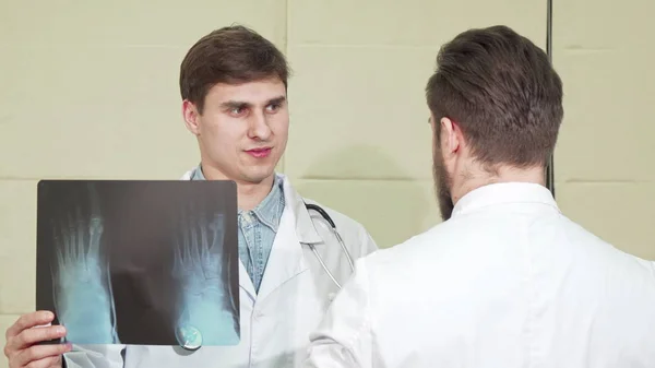 Όμορφος άντρας γιατρός που συζητάει με ακτινογραφία ποδιού με τον συνάδελφό του — Φωτογραφία Αρχείου