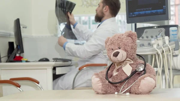 Pediatra maschio esaminando la risonanza magnetica, peluche orsacchiotto giocattolo in primo piano — Foto Stock