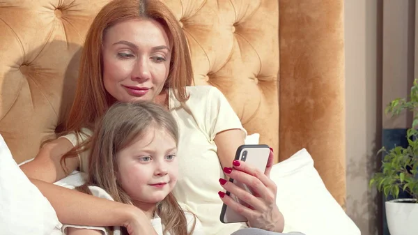 Mooie vrouw en haar schattige kleine dochter met behulp van slimme telefoon thuis samen — Stockfoto