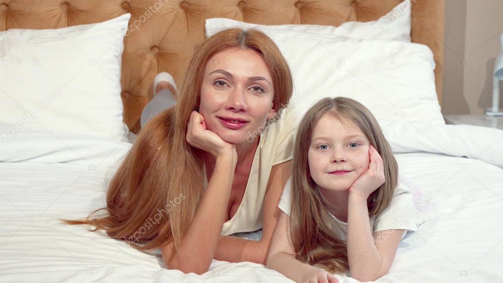 Mother and daughter smiling to the camera, lying on bed together