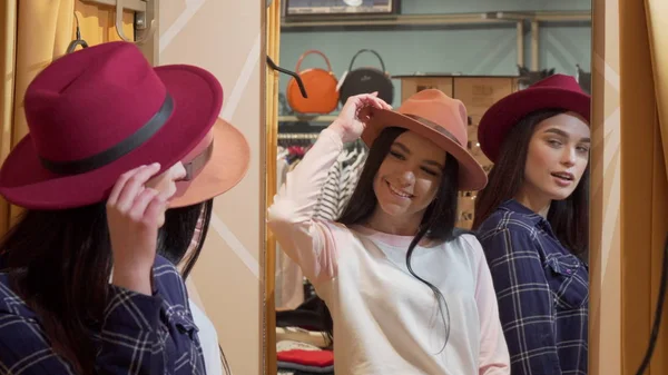Due giovani donne adorabili che provano cappelli, mentre fanno shopping insieme — Foto Stock