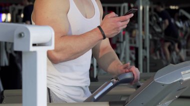 Spor salonunda bir koşu bandı üzerinde yürürken, akıllı telefon kullanarak tanınmayan adam