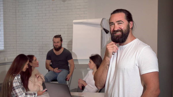 Зрелый красивый бородатый бизнесмен задумчиво улыбается в камеру
