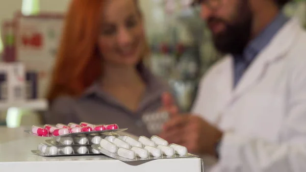 Farmacéutico tomando ampollas de pastillas del mostrador, hablando con su cliente femenino — Foto de Stock