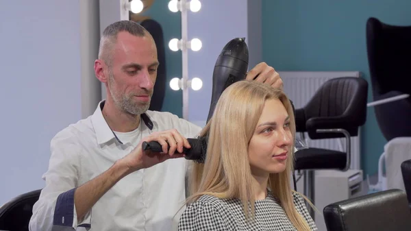 Зрелый мужчина парикмахер высушивает волосы клиентки в салоне — стоковое фото
