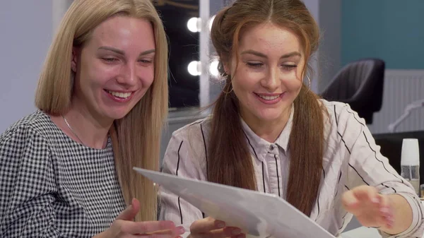 Twee vriendinnen onderzoeken haarkleur kleurstof grafiek bij beauty salon — Stockfoto